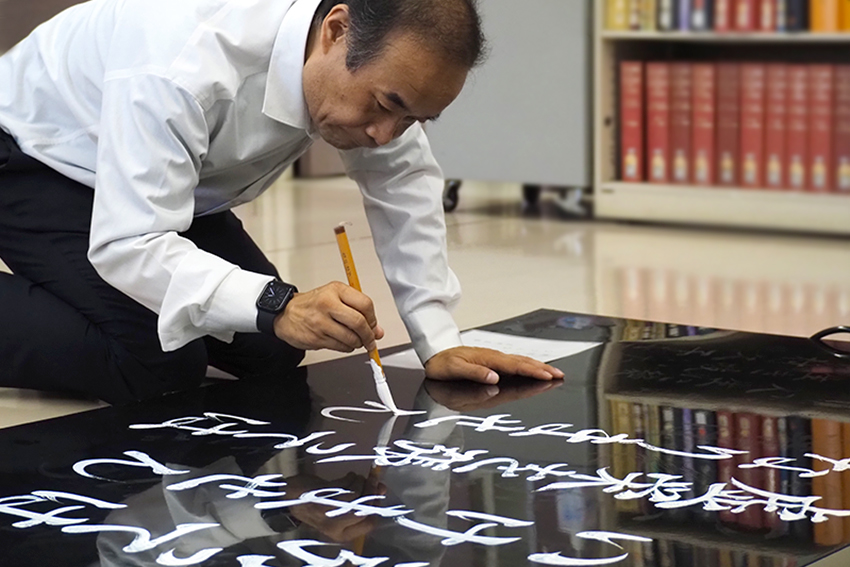 8月の聖語を揮毫する通信教育部 人間科学部 人間科学科仏教学専攻の前田壽雄先生。迷いなく一気に書き上げる